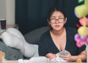 tired mother bottlefeeding newborn by Chanintorn.v shutterstock_2005671818-min very tired mother, squints at viewer, while she bottlefeeds her newborn at night