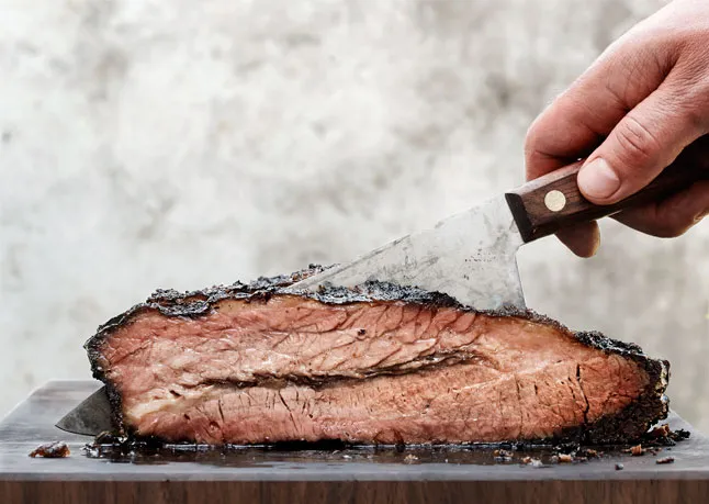 Side view of a person slicing into a juicy smoked brisket.