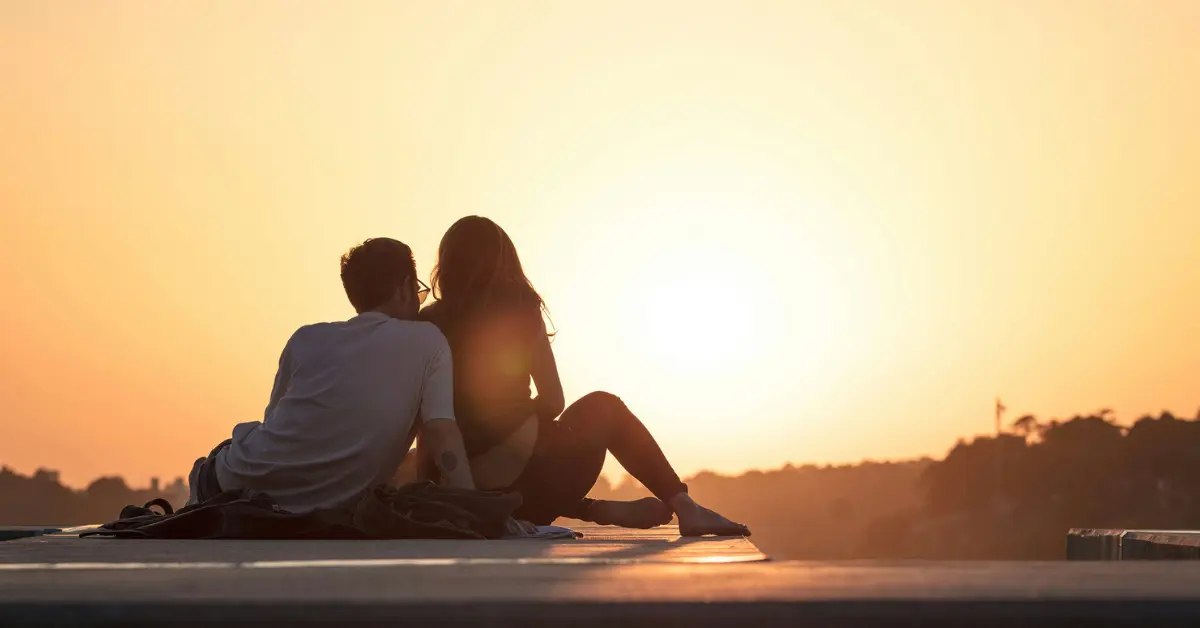 A couple sits close together while watching the sunset 