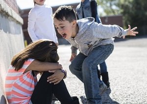 young boy aggressively taunting seated girl on the playground