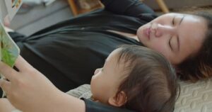 baby sleep tips mother reading to baby by HarryKiiM Stock shutterstock_2337401743-min mother reading to infant in bed, quiet and calm time together