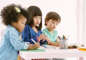three preschoolers standing at a table drawing pictures