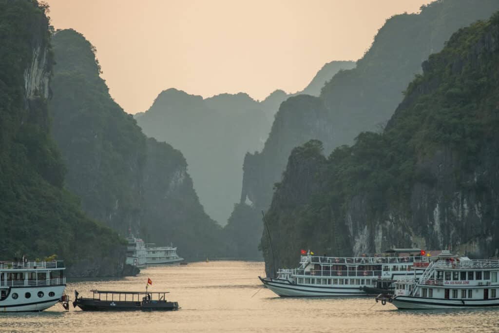 Touristenboote und Dschunken zwischen den Karstfelsen der Halong-Bucht in Vietnam im Abendlicht