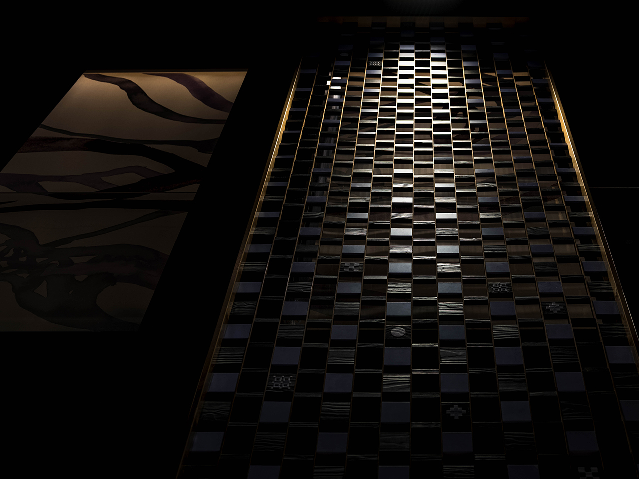 A dark, vertically oriented image shows a grid of black and dark gray tiles with subtle checkerboard patterns, bordered by panels with abstract, wavy designs.