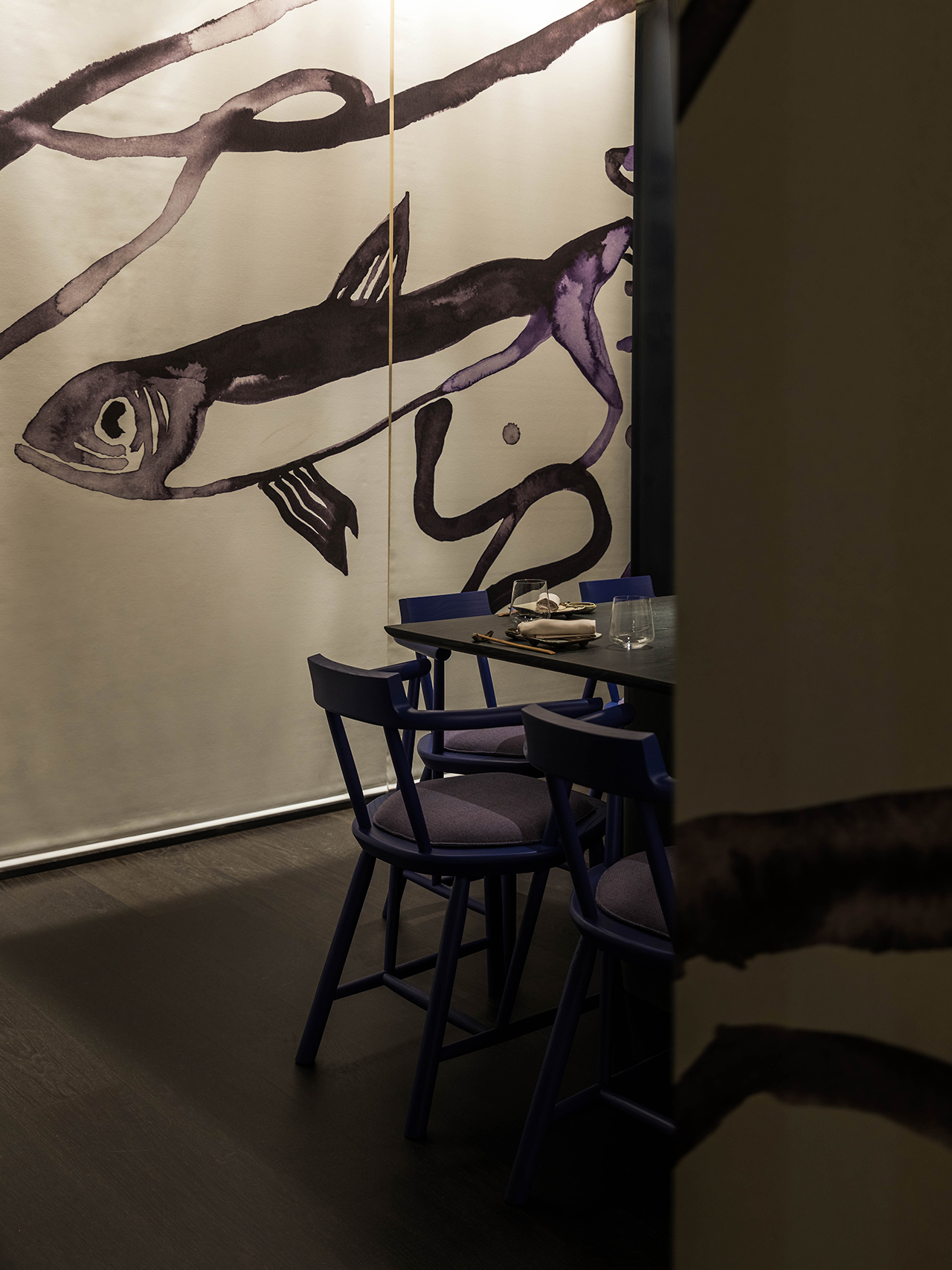 A dining area with a dark table and purple chairs, set against a wall featuring a large, abstract fish mural in black and purple tones.