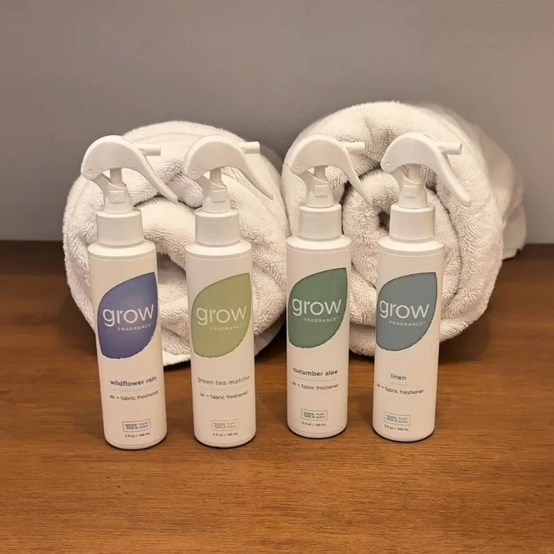 Four 'grow' home fragrance products on a wooden surface with towels in the background.
