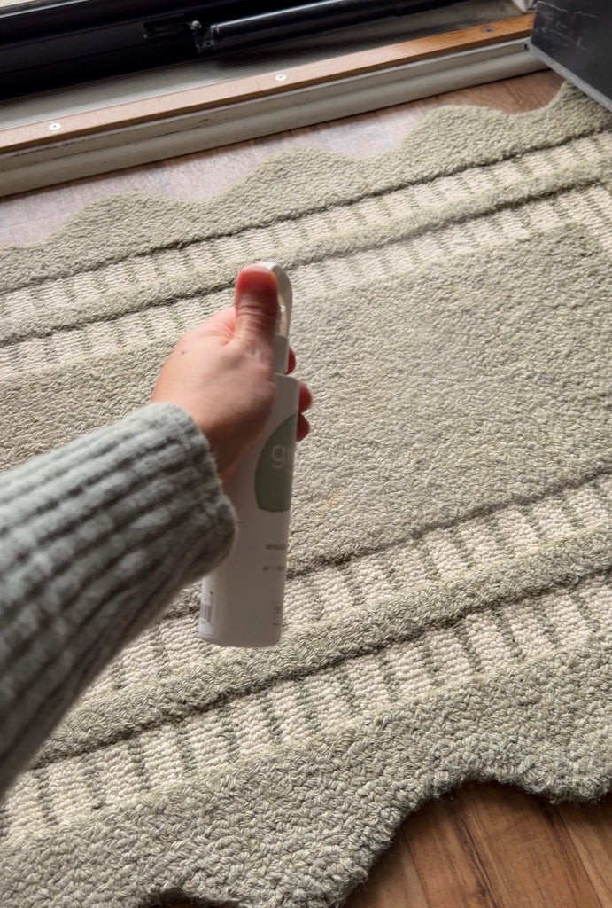 Hand holding a Grow Fragrance air and fabric freshener on a textured rug