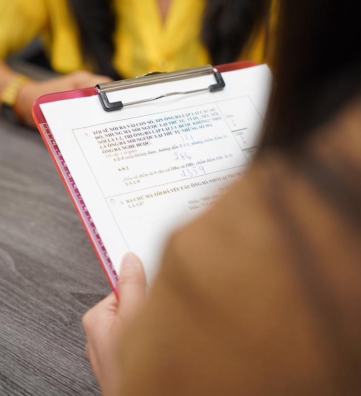 Person holds a clipboard with a Vietnamese-language cognitive assessment questionnaire during a research interview