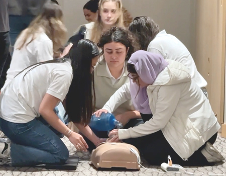 A group of students kneel next to a mannikin torso in a medical school classroom to learn CPR skills