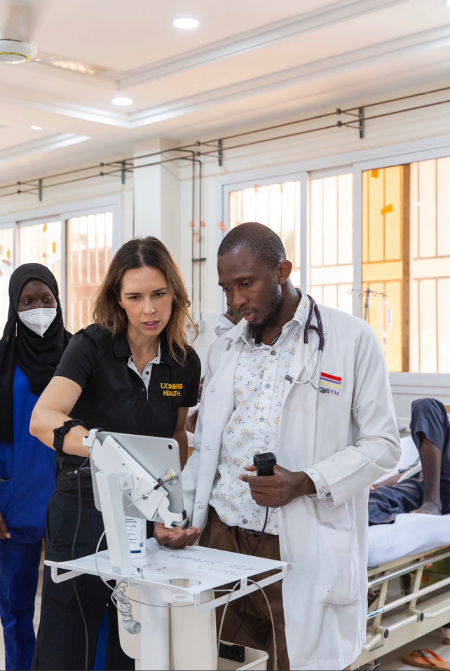 A healthcare trainer in a medical education program demonstrates a portable ultrasound device to a clinician in a hospital ward