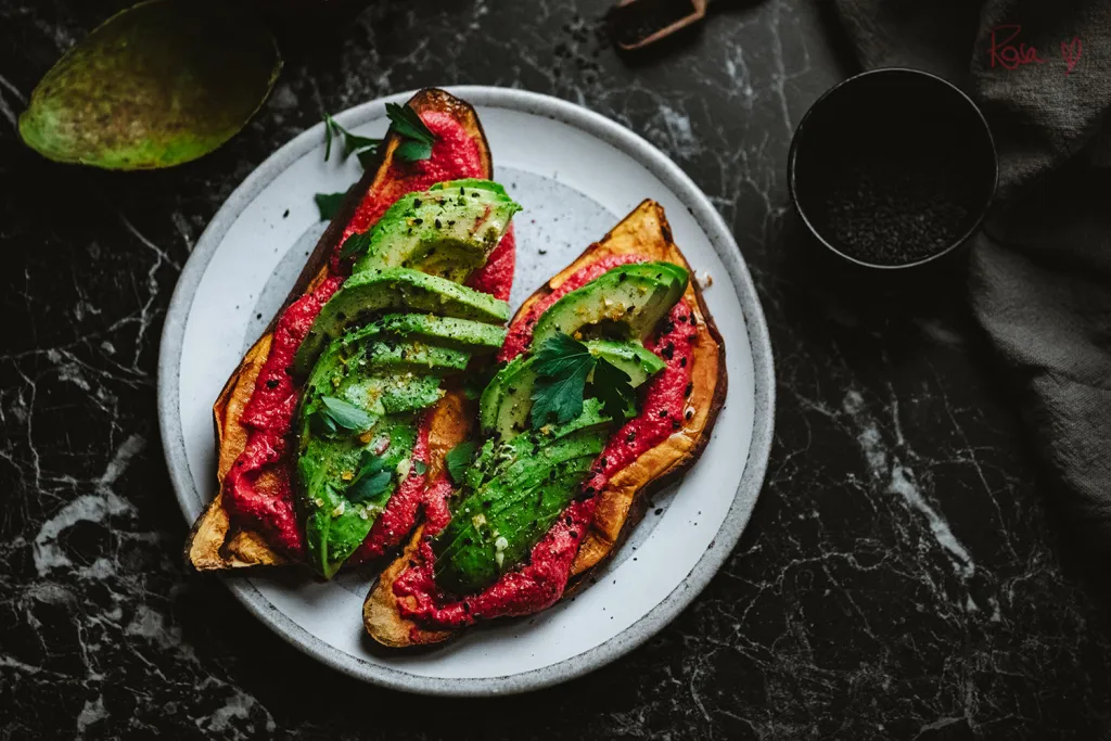Vegan sweet potato toasts topped with creamy beetroot and white bean spread, avocado slices, and fresh herbs. Healthy, gluten-free, high in fiber and vitamin A.
