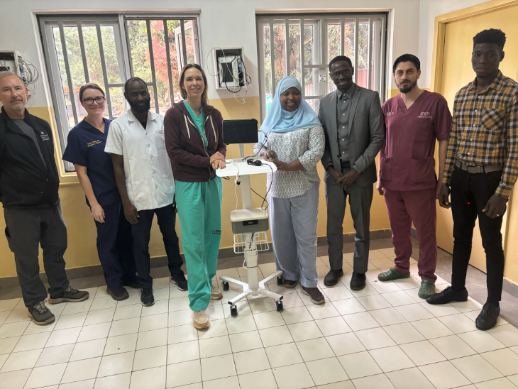 Healthcare professionals and partners surround a portable ultrasound machine in a clinical setting 