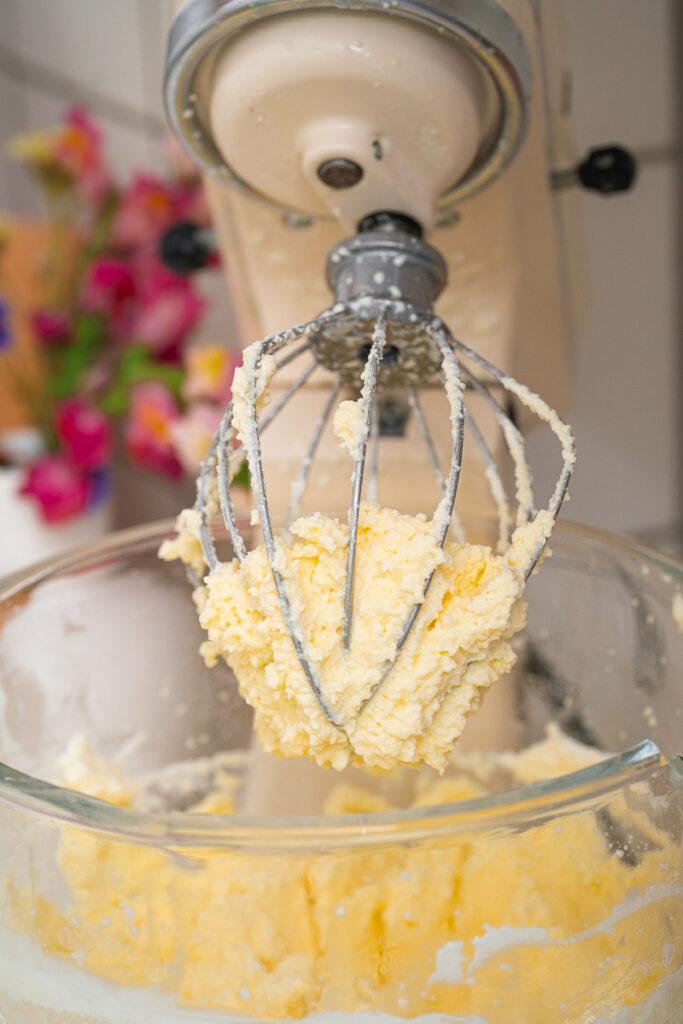 A pastry robot equipped with a whisk is holding a ball of freshly mixed butter over a glass mixing bowl.