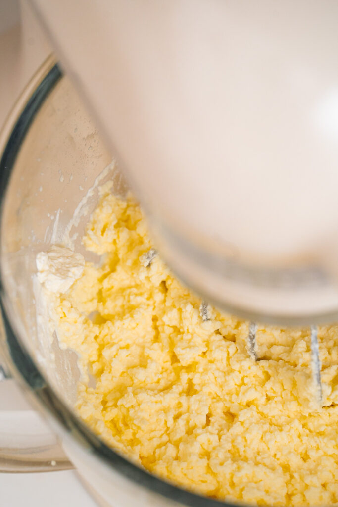 Seen from above, we can see yellow dough being kneaded in a stand mixer equipped with a glass bowl.