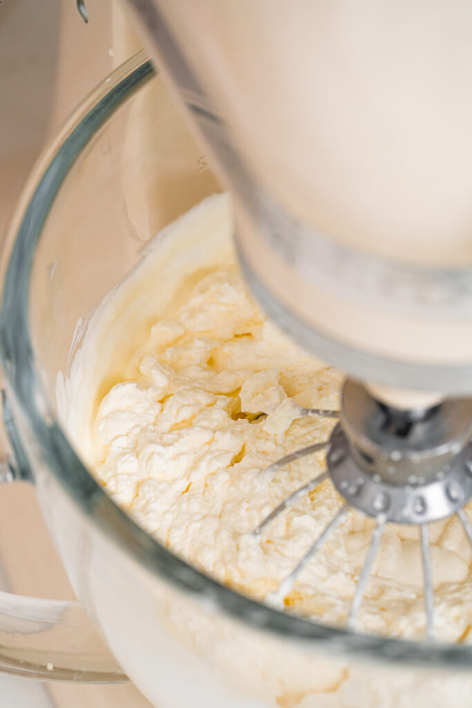An electric mixer whips cream in a clear glass bowl until it reaches a light and creamy consistency.