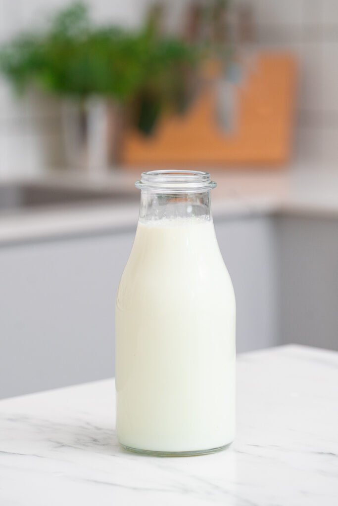 A clear glass bottle filled with milk sits on a white marble countertop in a modern-style kitchen.