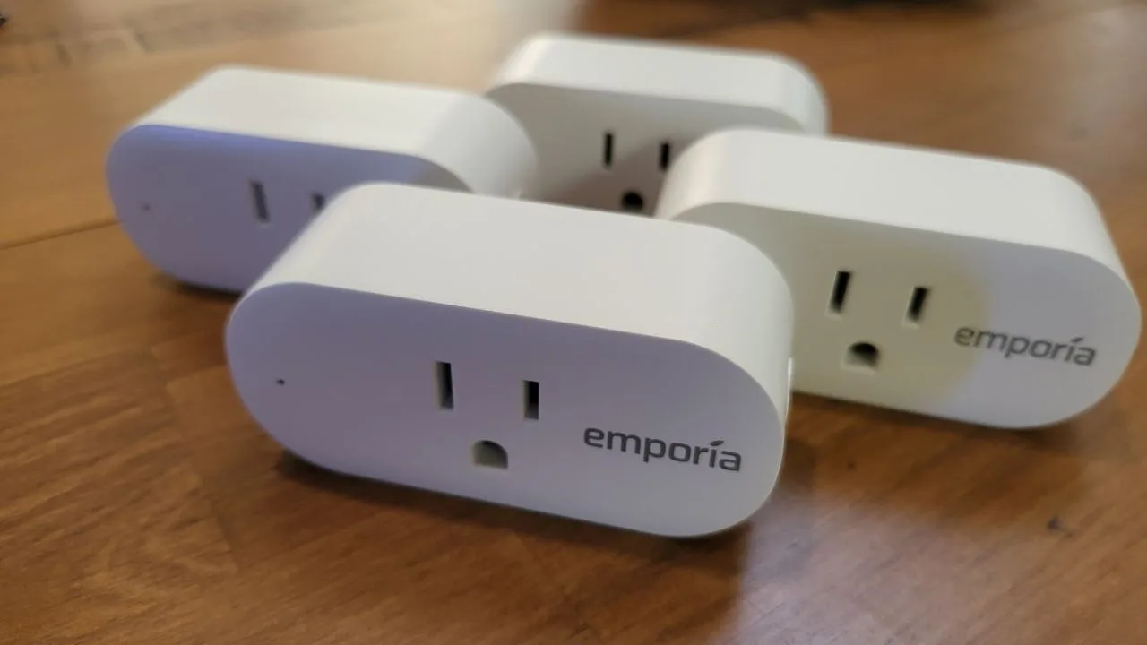 Vier Emporia Smart Plugs auf einem Holztisch.