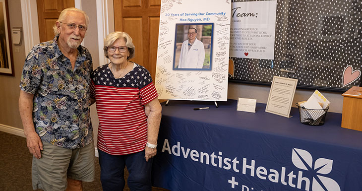 Ein Mann und eine Frau stehen neben einem Tisch mit einem Adventist Health-Schild und einem Plakat zur Feier der Dienstjahre von Dr. Hoa Nguyen. 